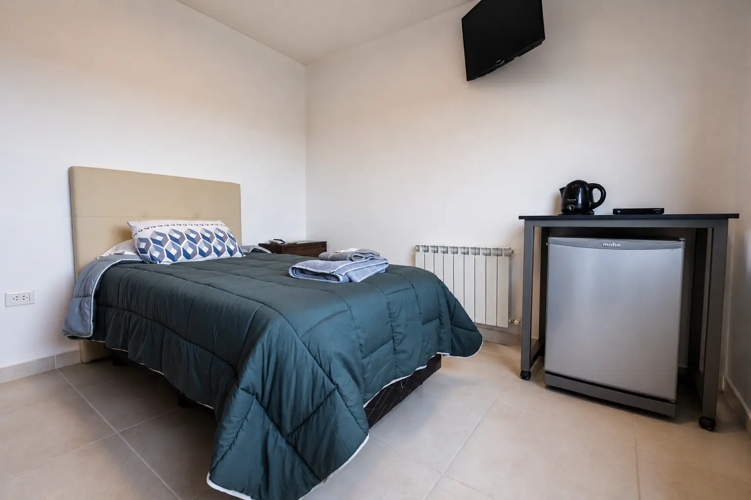 Detalle de la ropa de cama y la mesa de luz de una habitación.